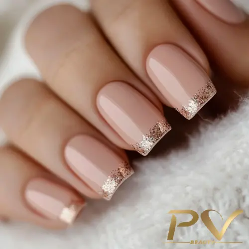 Unhas com esmalte nude e pontas decoradas com glitter dourado.