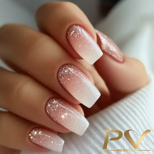 Mão com unhas decoradas em degrade rosa e branco, com glitter brilhante.