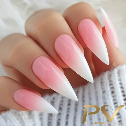 Unhas em formato stiletto com esmalte em degradê rosa e branco, mão segurando uma blusa de tricô branca.