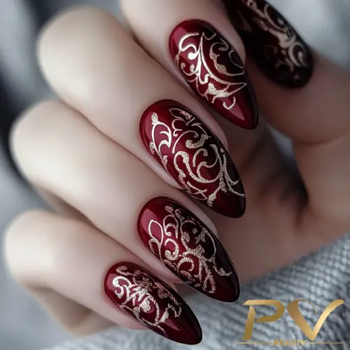 unhas-vinho-decoradas-arabescos-brilhantes-pv-beauty-14 Unhas decoradas com esmalte vermelho escuro e detalhes dourados em um padrão intricado de arabescos.