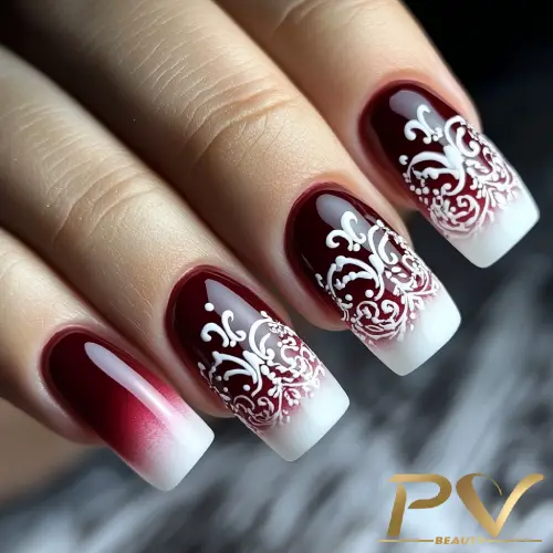 unhas-vinho-decoradas-arabescos-pv-beauty-06 Unhas decoradas com esmalte vermelho e branco, apresentando um design floral intrincado nas pontas.