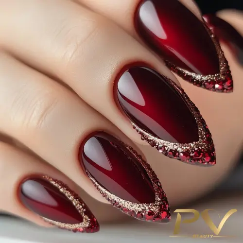 unhas-vinho-decoradas-glitter-strass-pv-beauty-15 Unhas compridas e pontiagudas com esmalte vermelho escuro e detalhes brilhantes nas bordas.