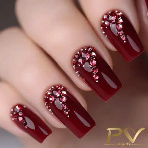 unhas-vinho-decoradas-pedrarias-elegantes-pv-beauty-13 Unhas decoradas com esmalte vermelho escuro e pedras brilhantes prateadas e vermelhas na base.