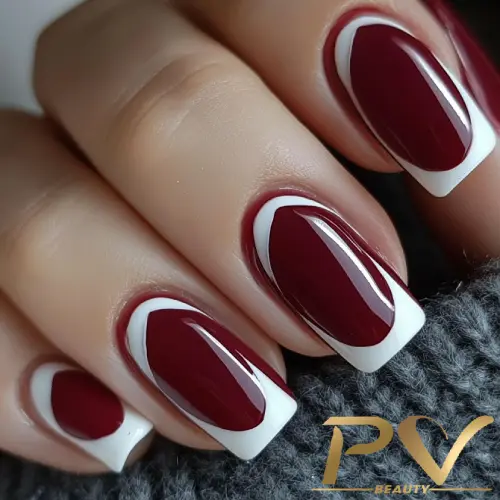 unhas-vinho-francesinha-decoradas-pv-beauty-29 Mão com unhas decoradas em esmalte vermelho e branco, sobre tecido cinza, mostrando estilo de manicure.