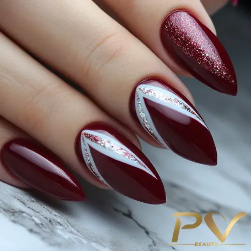 unhas-vinho-glitter-decoradas-pv-beauty-25 Unhas com esmalte vermelho e detalhes prateados e brancos, em formato estilete, sobre superfície marmorizada.