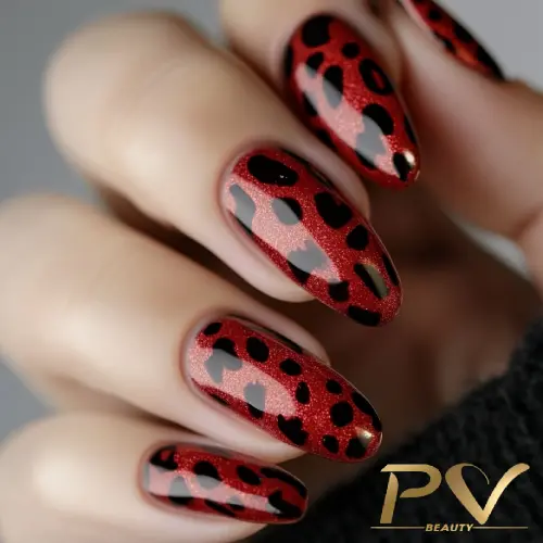 unhas-vinho-oncinha-animal-print-decoradas-pv-beauty-10 Mãos com unhas longas decoradas com esmalte vermelho e preto, com padrão de manchas.