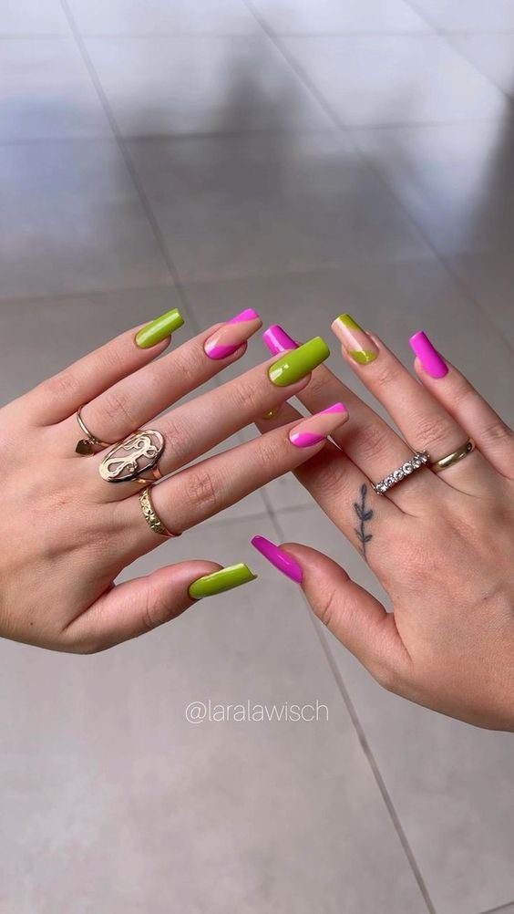 verde-e-rosa-tambem-e-uma-boa-combinacao Mãos com unhas longas pintadas de verde e rosa, adornadas com anéis e tatuagem de galho.