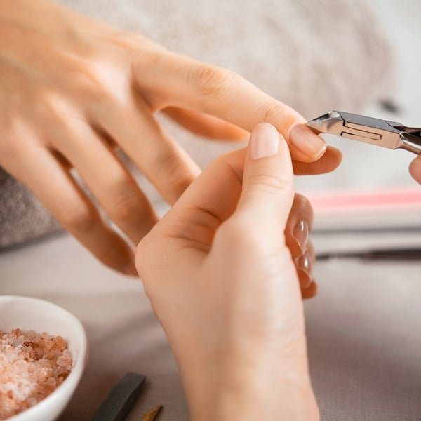 Manicure tirando a cutícula da cliente com alicate.