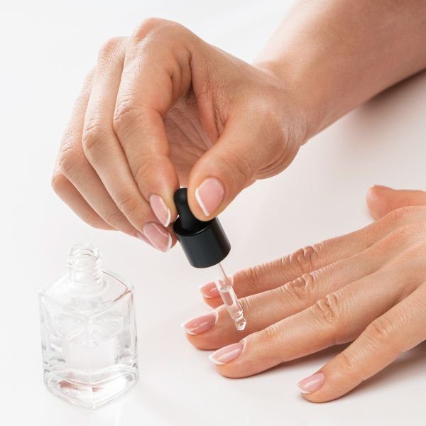 Mulher aplicando base para suas unhas segurando conta gotas.