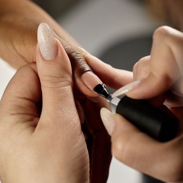 Mãos aplicando base para crescimento em unhas longas.