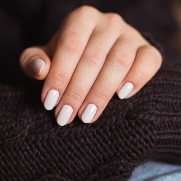 Mão com Old Money Nails apoiada no braço com casaco marrom.