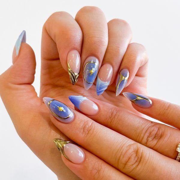 Mãos com press on nails com nail art nas unhas, com desenhos em dourado, esmaltação em tons azul e nude.