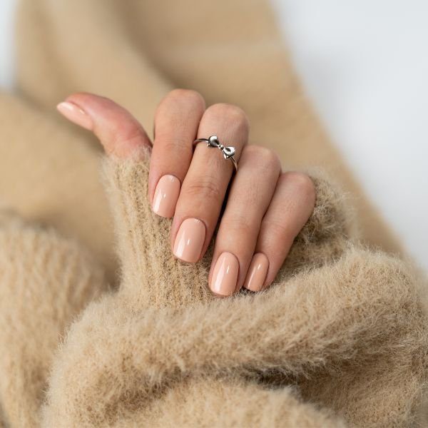 unha-clean-nude-perolado Mão com manga de casaco felpudo bege e unhas clean em tom nude perolado.