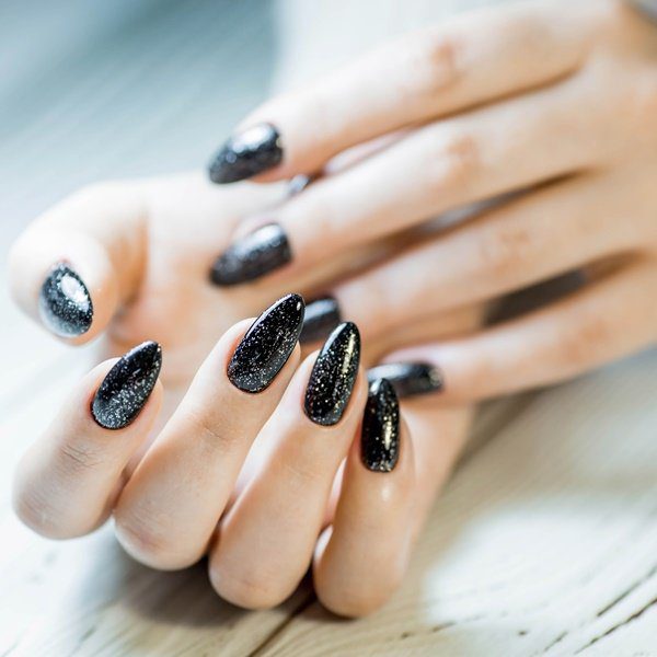 unha-encapsulada-preta-glitter Mão com unhas pretas encapsuladas com glitter prateado.