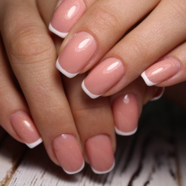 Mãos com unhas longas e quadradas com nail art de francesinha rosa e branco.